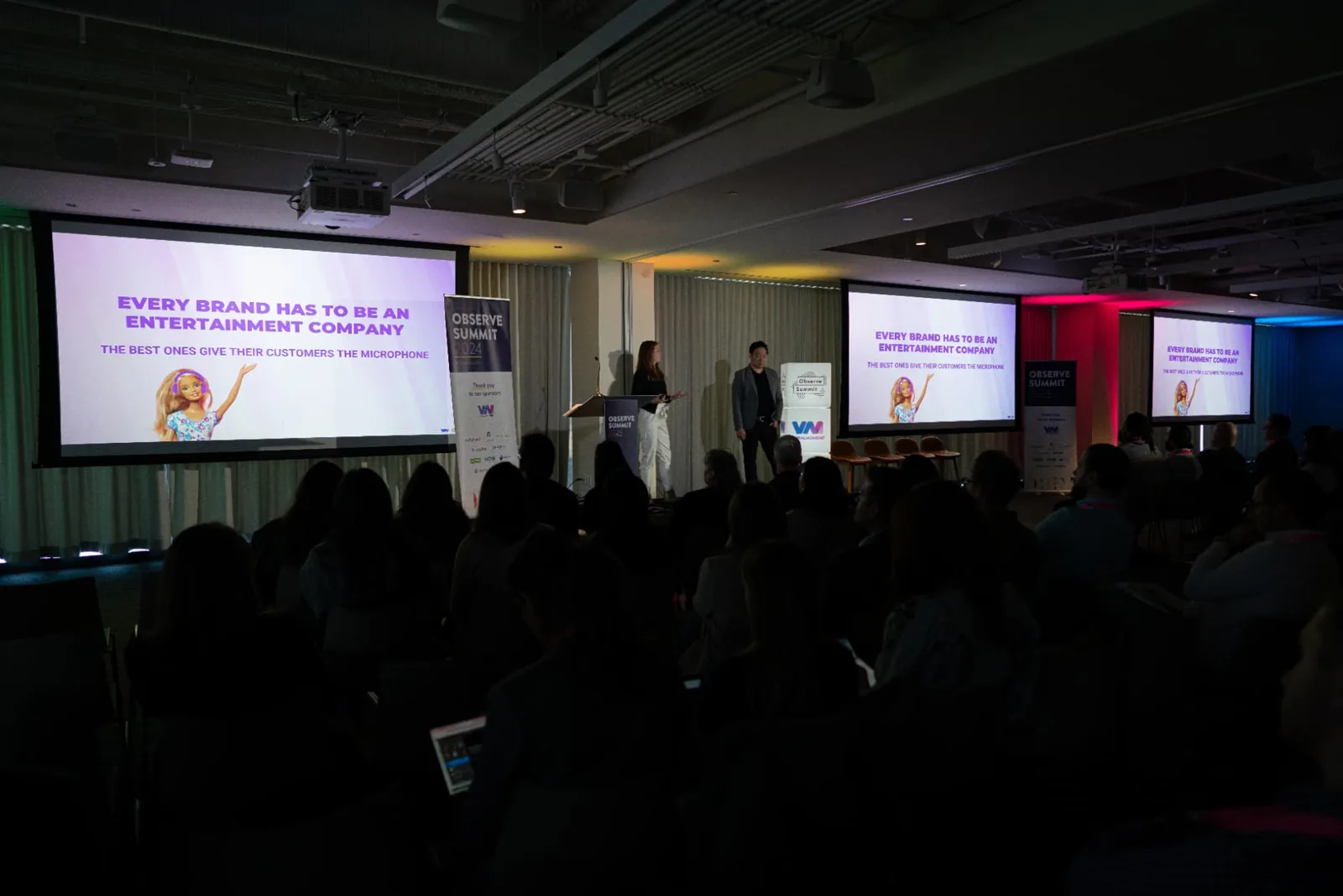 Elizabeth Arnold presenting on stage beside another speaker to a seated audience